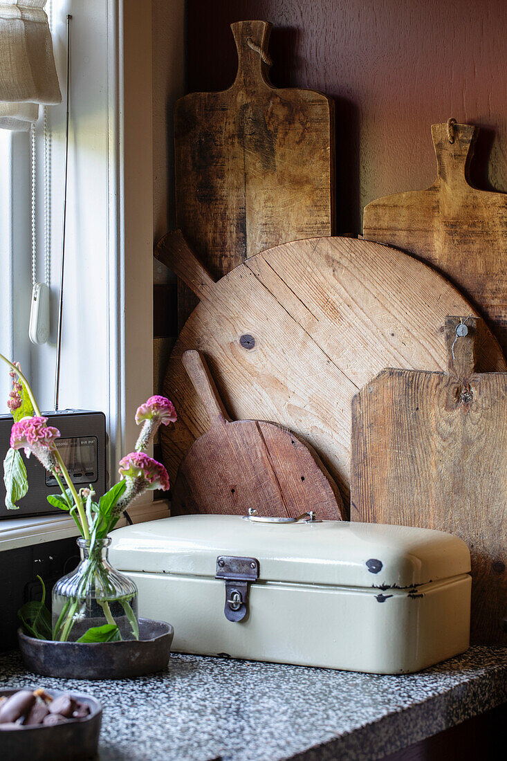 Vintage bread bin and chopping boards on kitchen counter in front of red-brown wall