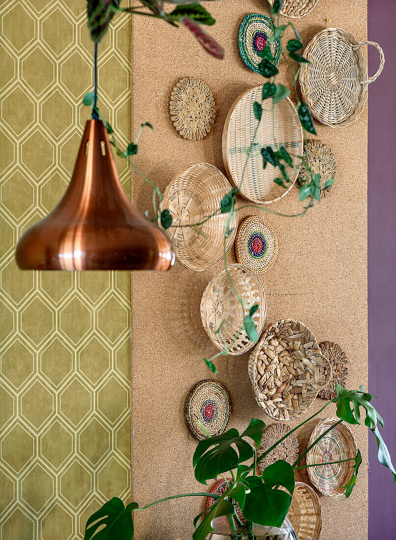 Wall decoration made of woven baskets next to copper lamp and monstera plant