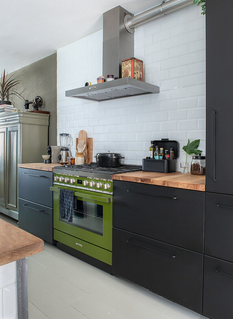 Black kitchen cupboards with green oven and wooden counters against a white tiled wall