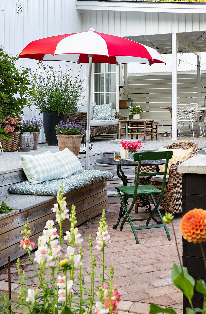 Gartenbereich mit Terrassenmöbeln, bunten Blumen und rot-weißem Sonnenschirm