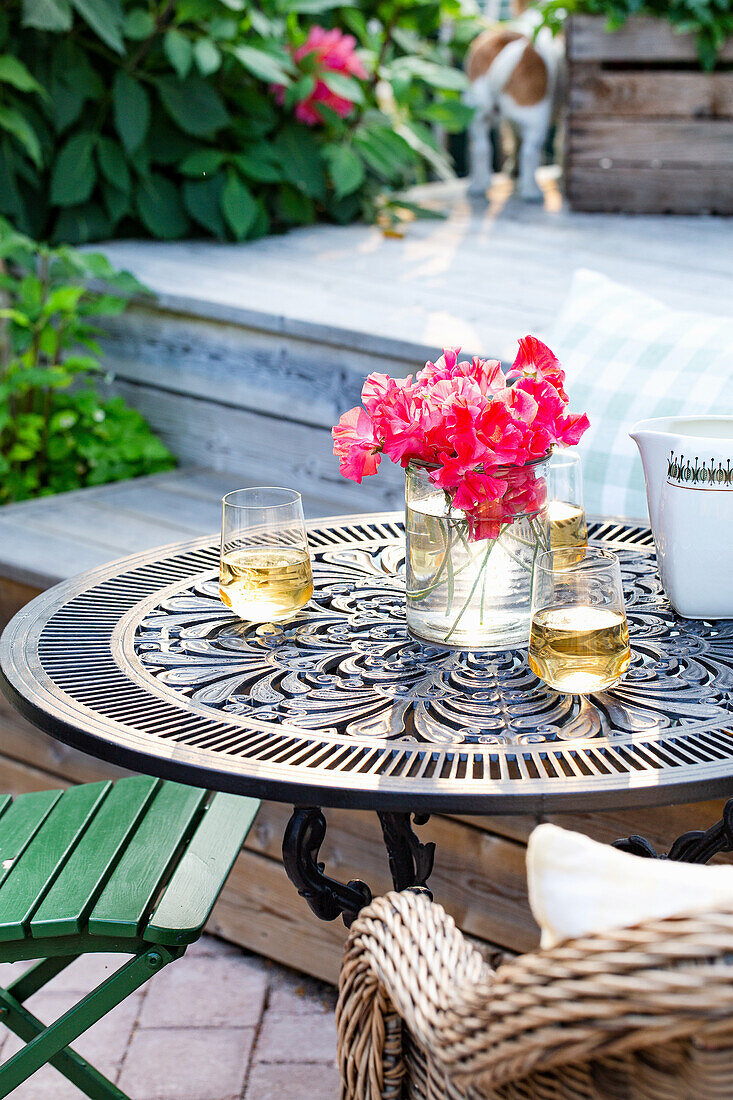 Runder Metalltisch mit rosa Blumenstrauß und Getränken auf Terrasse im Abendlicht