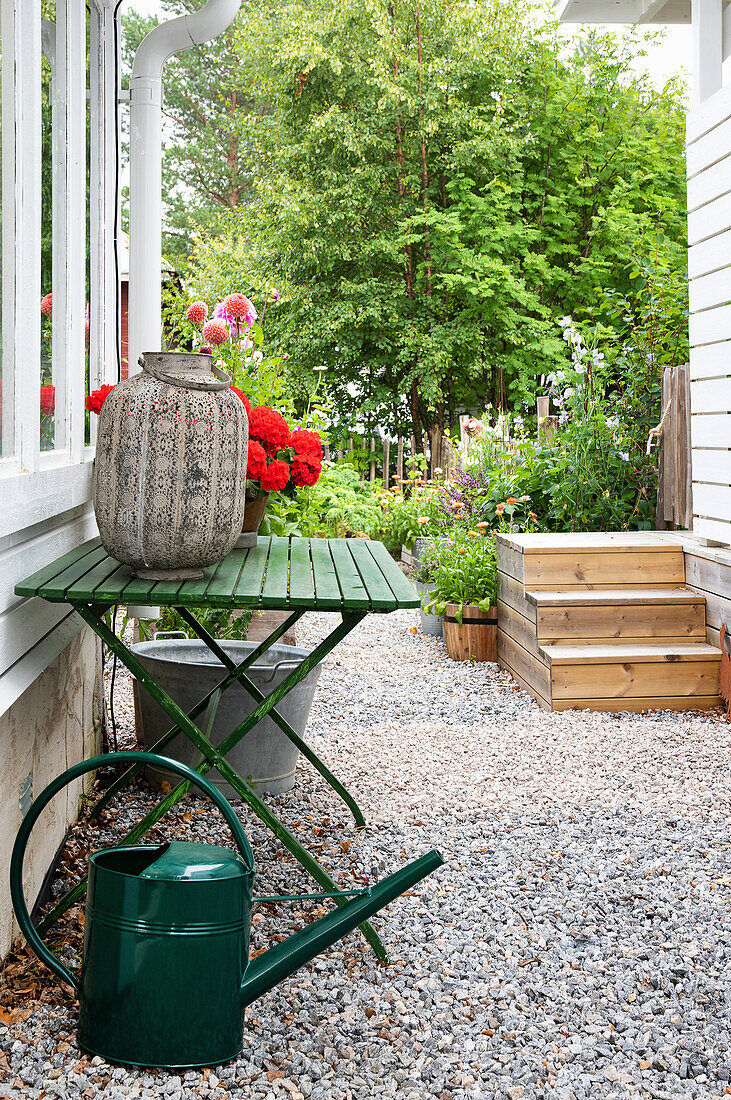 Green folding table with vase and watering can on gravel path in garden