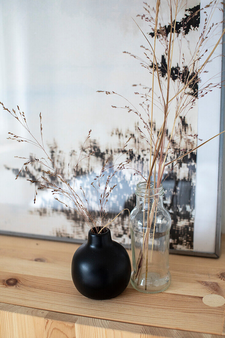 Schwarze Kugelvase und Glasflasche mit getrockneten Gräsern auf Holztisch