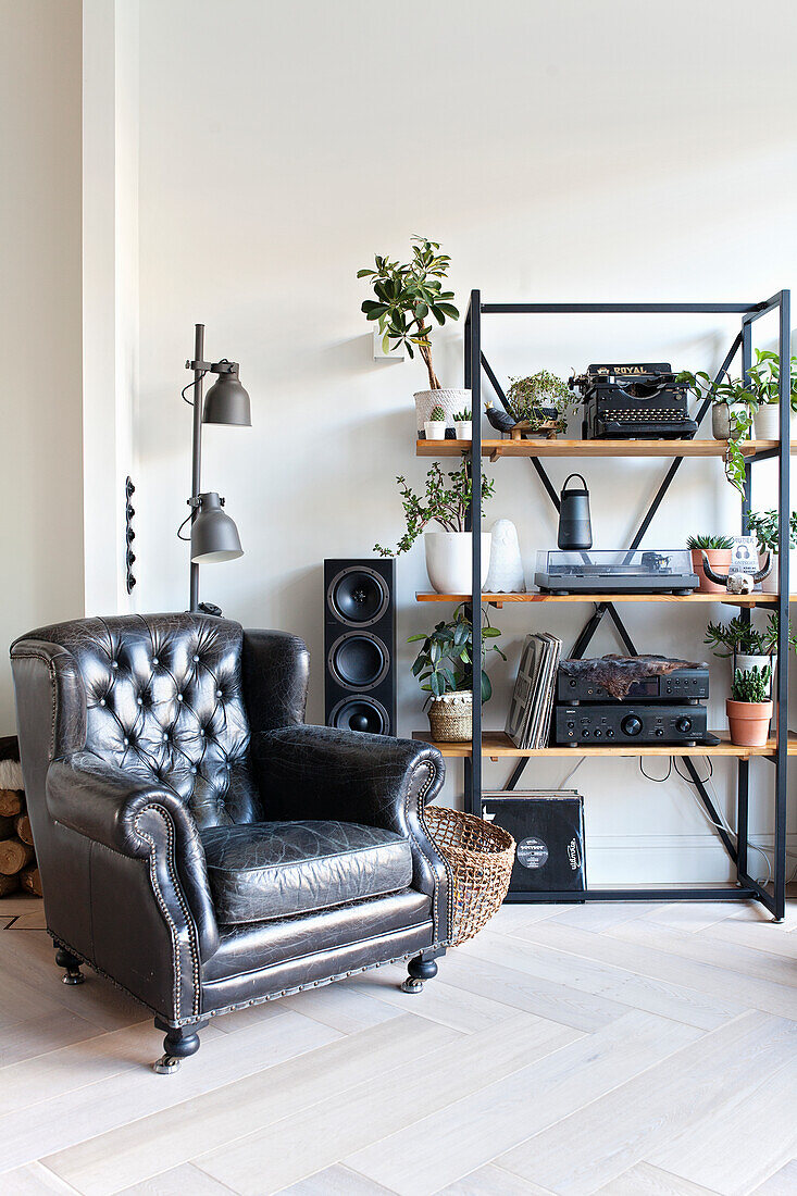 Black leather armchair next to metal shelf with plants and retro decorations