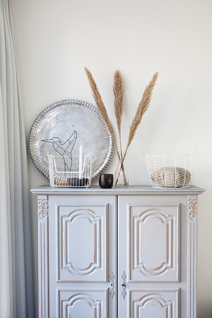 Vintage-Sideboard mit Deko-Tablett, Ziergras und Drahtkörben im Wohnzimmer