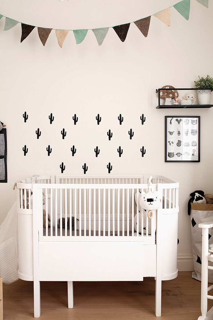 Small white baby cot with cactus wall stickers in the nursery