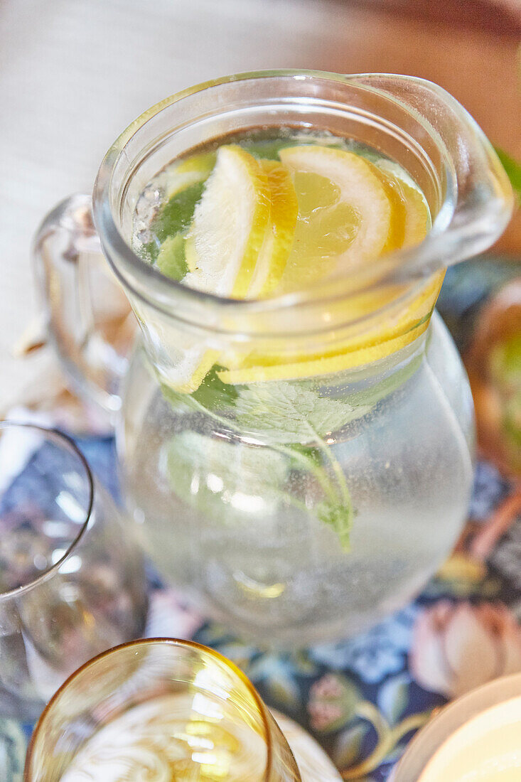 Glas-Karaffe mit Zitronenwasser auf einem bunt gemusterten Tischtuch