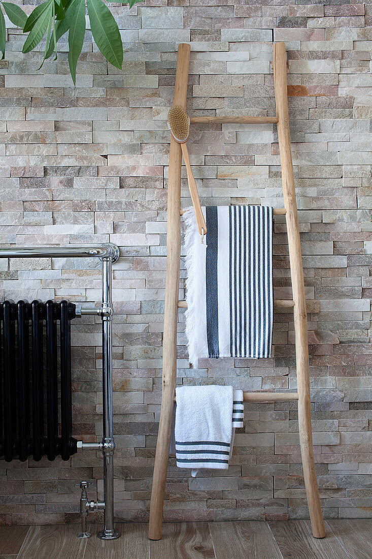 Wooden ladder towel rail in front of stone wall in modern bathroom