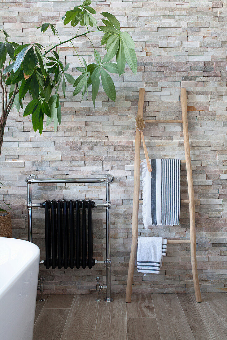 Modern bathroom with natural stone wall, black radiator and wooden ladder as towel rail