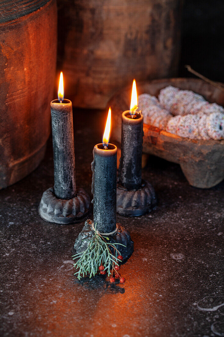 Three black stick candles with a fir branch on a dark stone table