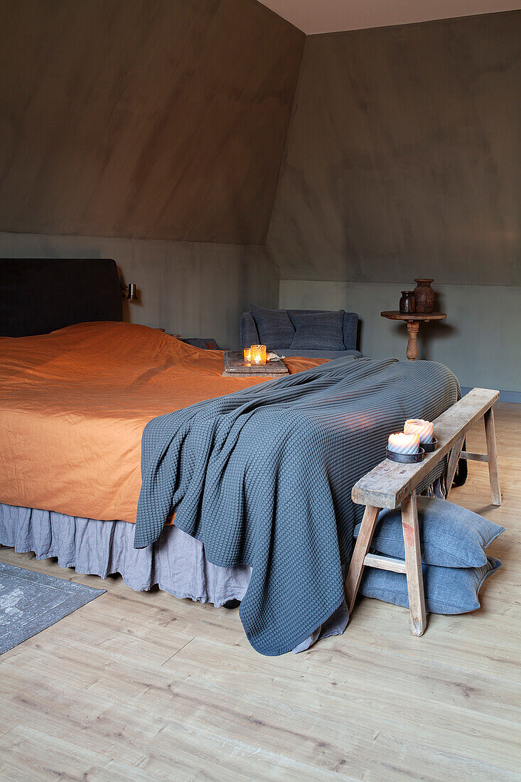 Schlafzimmer mit schräger Decke, hellem Holzboden und rustikalem Holzhocker