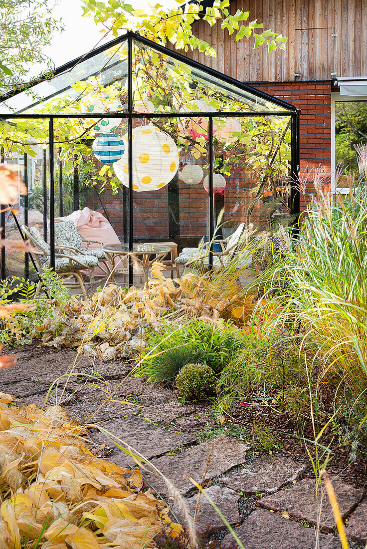 Gemütlicher Sitzbereich im verglasten Gartenpavillon mit Herbstpflanzen