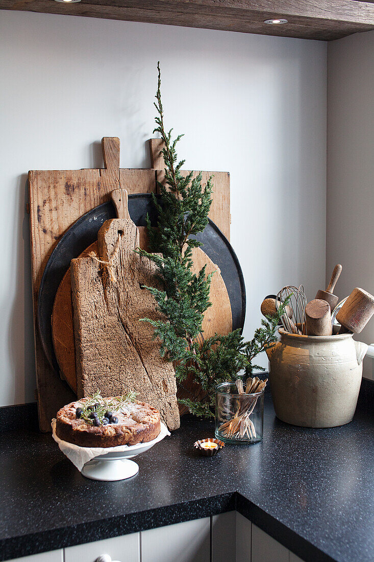 Ländlich dekorierte Küchenecke mit Holzbrett, Küchenuntensilien und Wacholderzweig