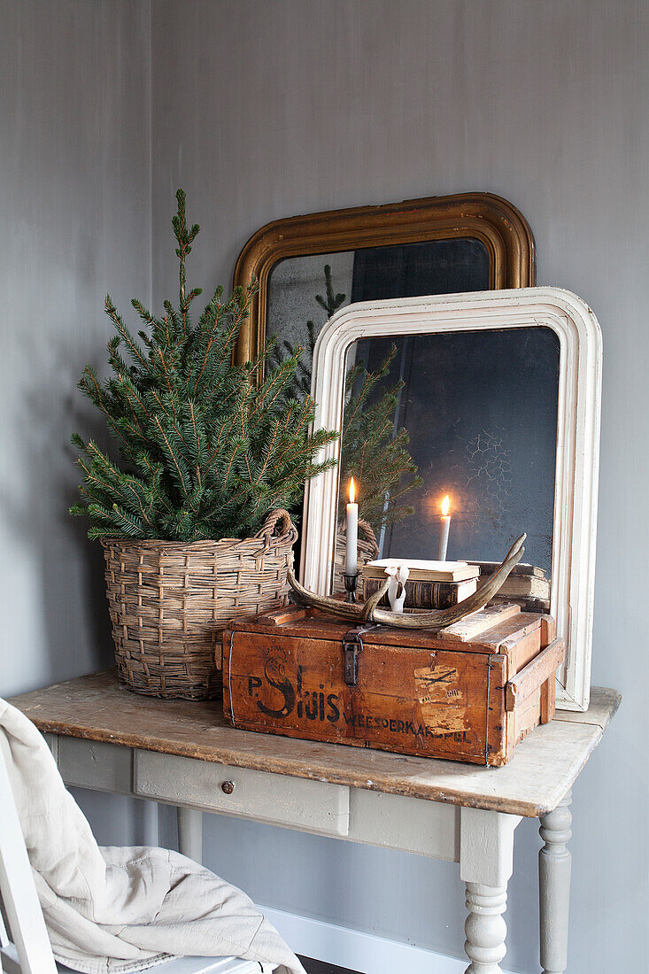 Decorative table with Christmas tree in basket, old mirrors and wooden box