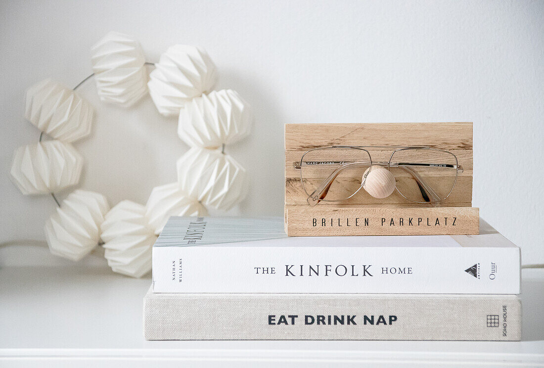 Wooden glasses holder on stack of books in front of white wall decoration