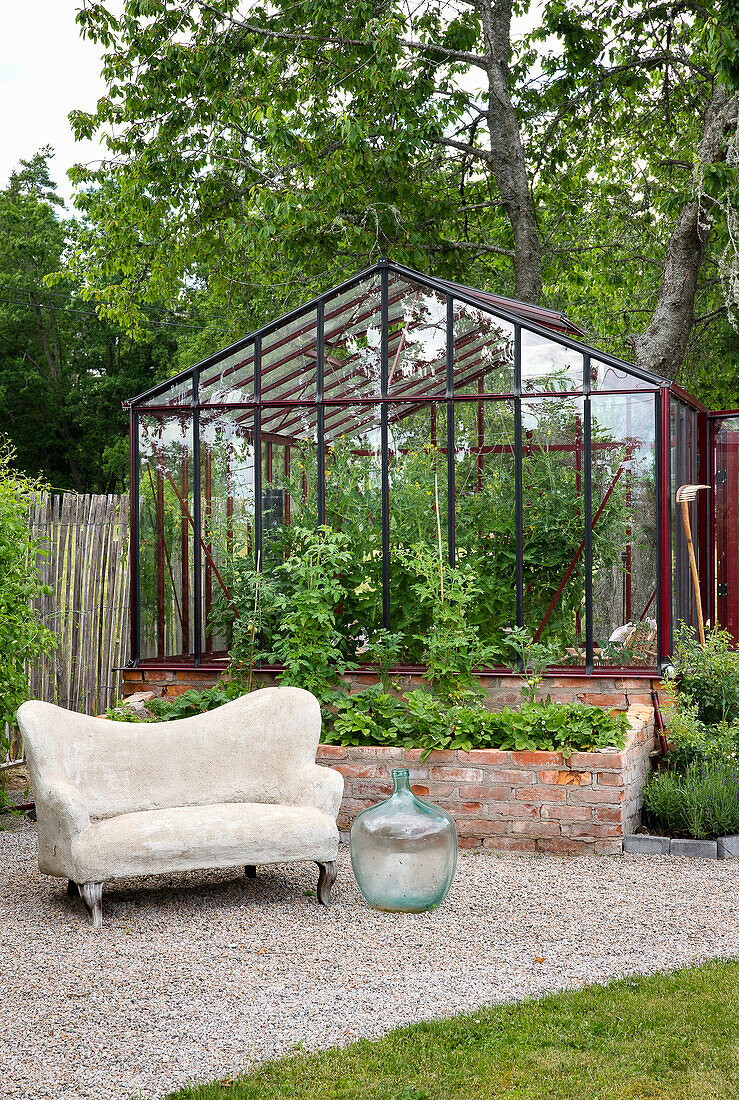 Garten mit Gewächshaus und Stein-Sofa vor Hochbeet aus Ziegelsteinen