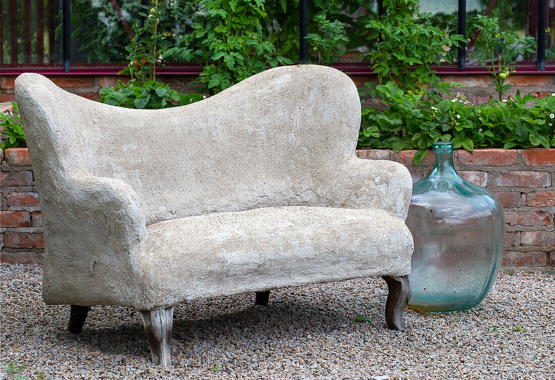 Steinbank und Glasflasche vor Backsteinmauer im Garten