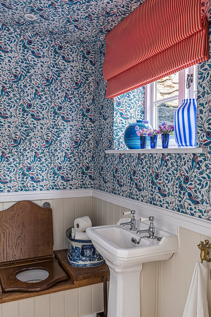Patterned wallpaper and blue ceramics in the rustic bathroom with wooden toilet