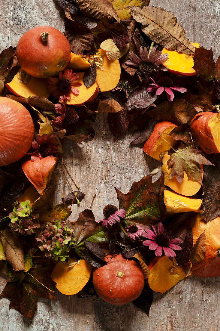 Herbstkranz mit Kürbisstücken, Blättern und Echinaceablüten auf Holzuntergrund