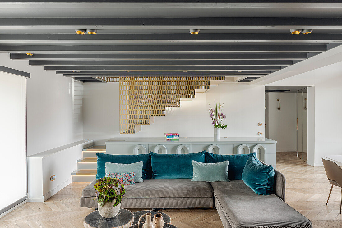 Open-plan living room with grey sofa and blue cushions, staircase with metal panelling