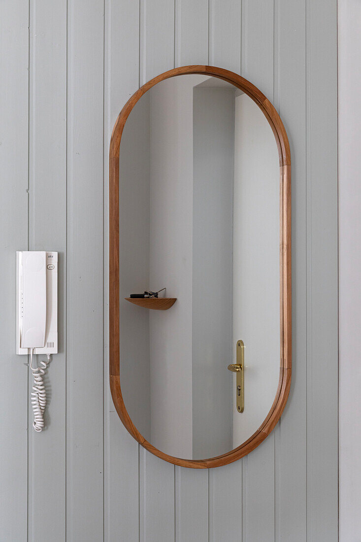 Oval wall mirror with wooden frame next to intercom system