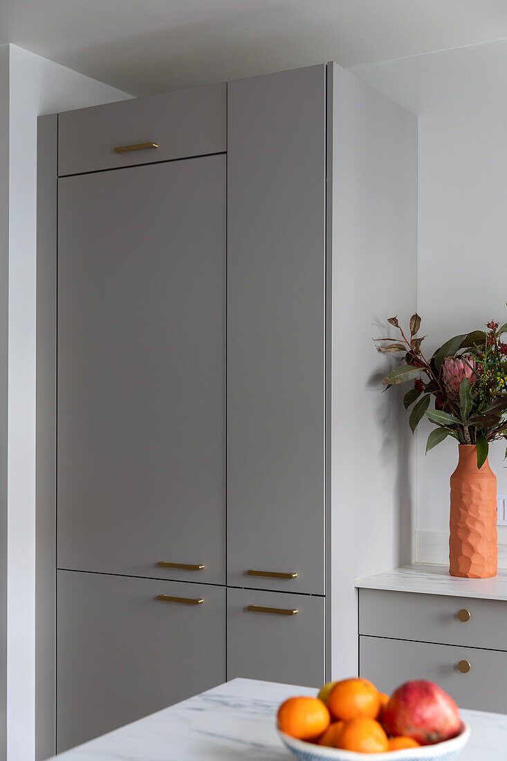 Grey fitted kitchen with golden handles and bouquet of flowers in modern vase