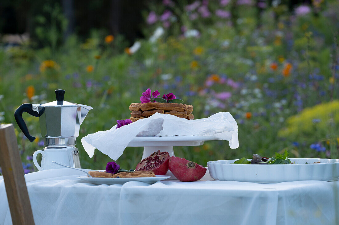 Frühstückstisch in bunter Blumenwiese mit Waffeln und Kaffee