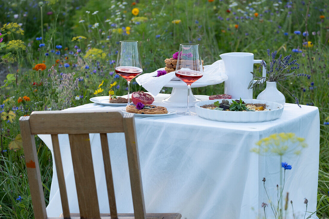 Set table with food and rosé wine in a meadow of flowers