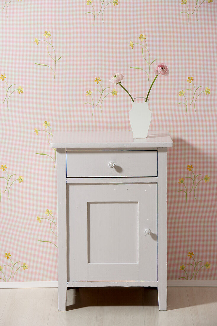 Kommode mit Vase und Ranunkeln, rosa Wand mit gelben Blumen