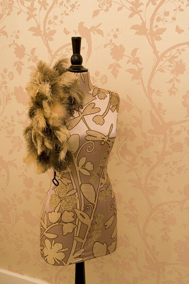 Dressmaker's dummy with silk fabric and feather boa in front of champagne-coloured silk wallpaper