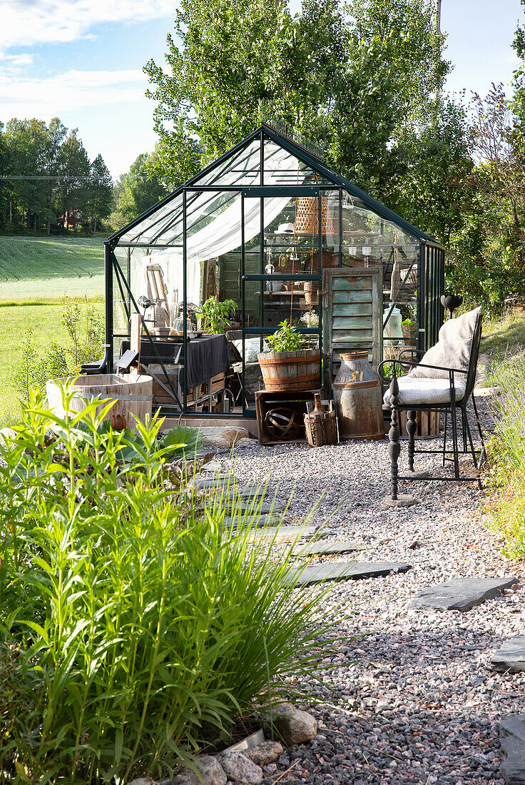 Weg aus Kies und Steinplatten führt zu Gewächshaus im Garten