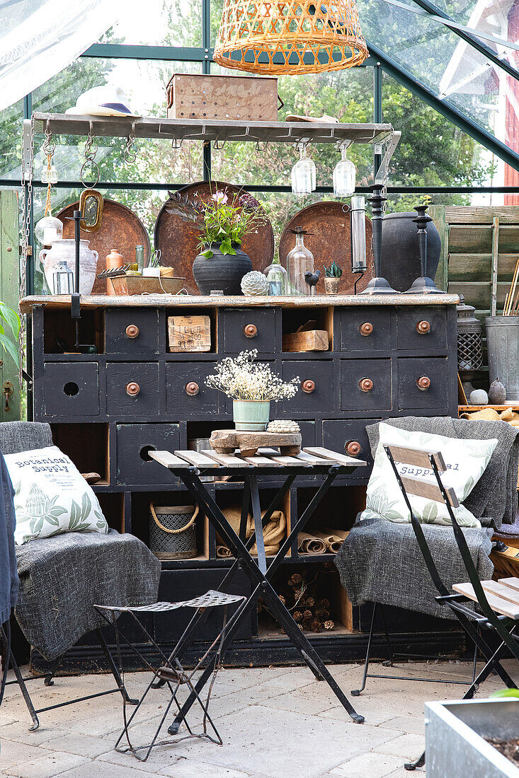 Greenhouse with antique apothecary cabinet, garden furniture and hanging lamp