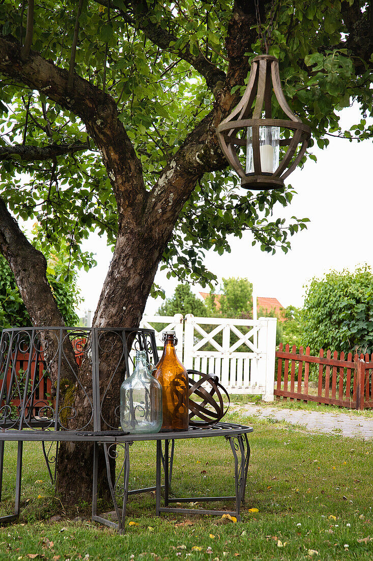 Vintage-Sitzbank unter Baum mit Dekoflaschen und Laterne im Garten