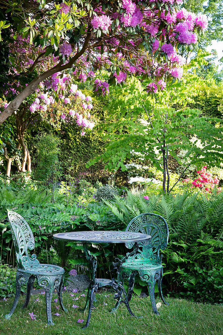 Romantic garden corner with cast-iron furniture under blooming rhododendrons