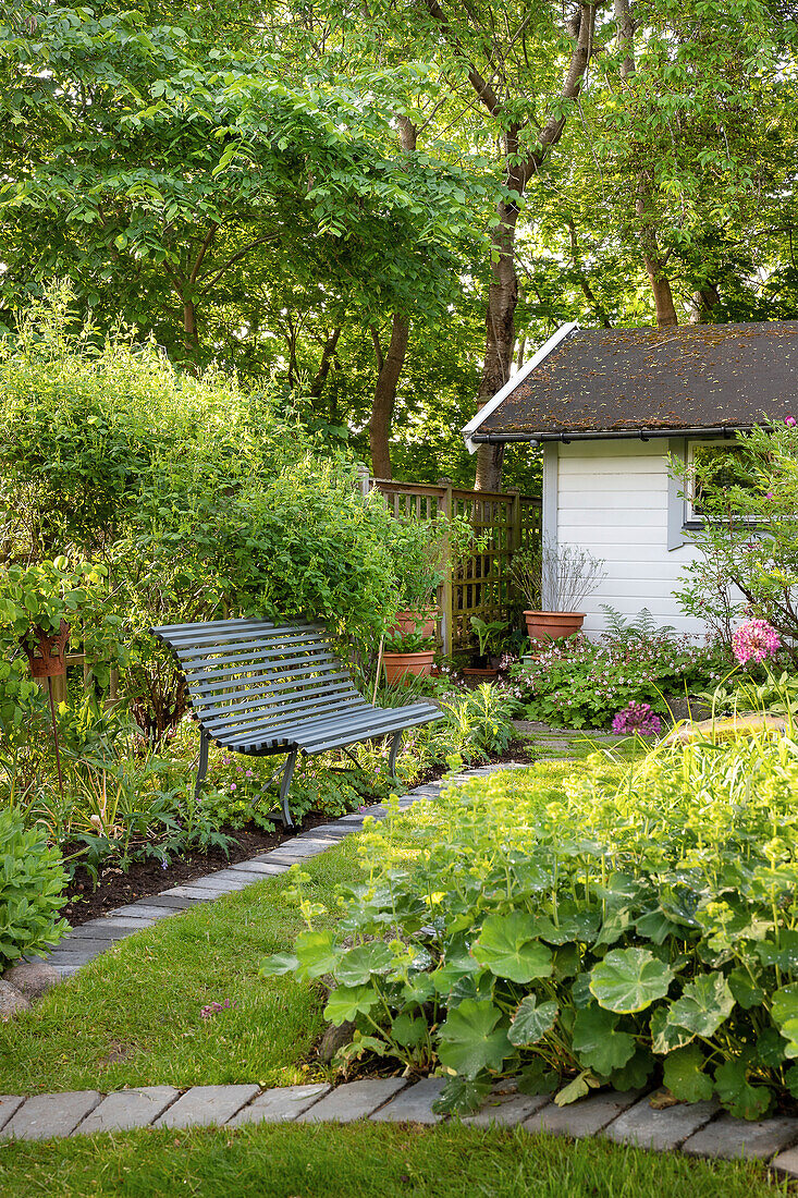 Metallbank und Gartenhaus umgeben von üppigem Grün im Sommergarten