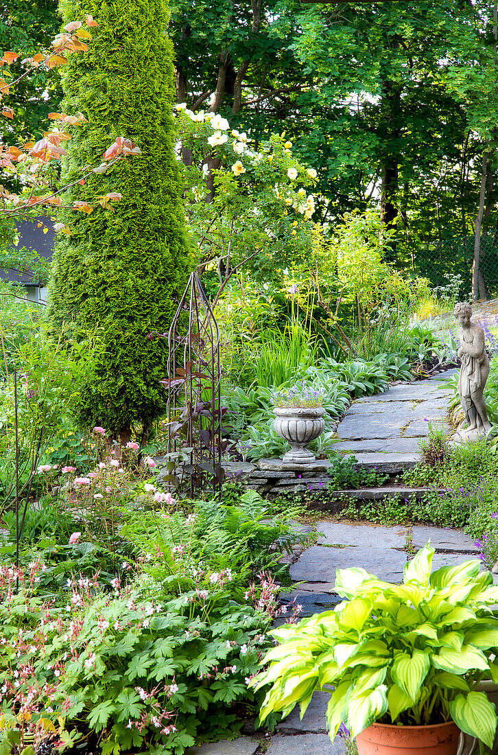 Blühender Gartenpfad mit Stauden, Steinweg und Steinfigur