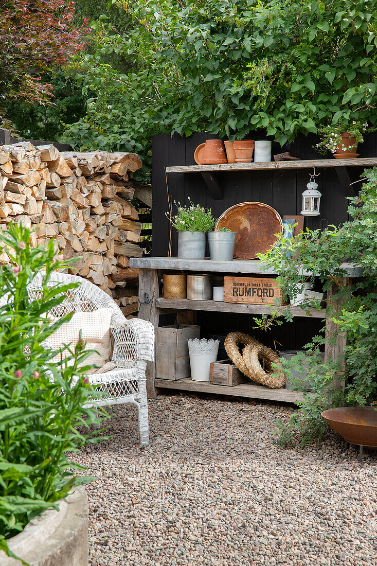 Gartenarbeitsplatz mit Regal, Kräutertöpfen und Holzlager auf Kiesweg