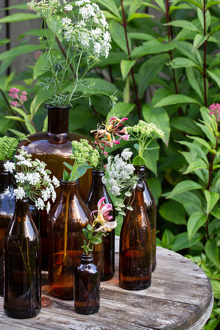 Braune Glasflaschen mit Wildblumen auf Holztisch im Garten