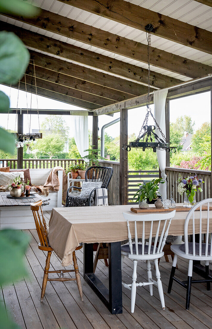 Covered wooden terrace with dining table, various chairs and seating area in the background