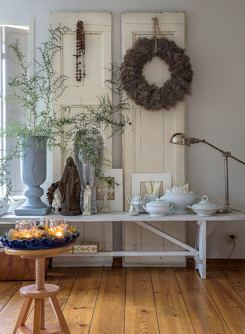 Decorative console table with candles, plants and wreath in front of white wooden doors