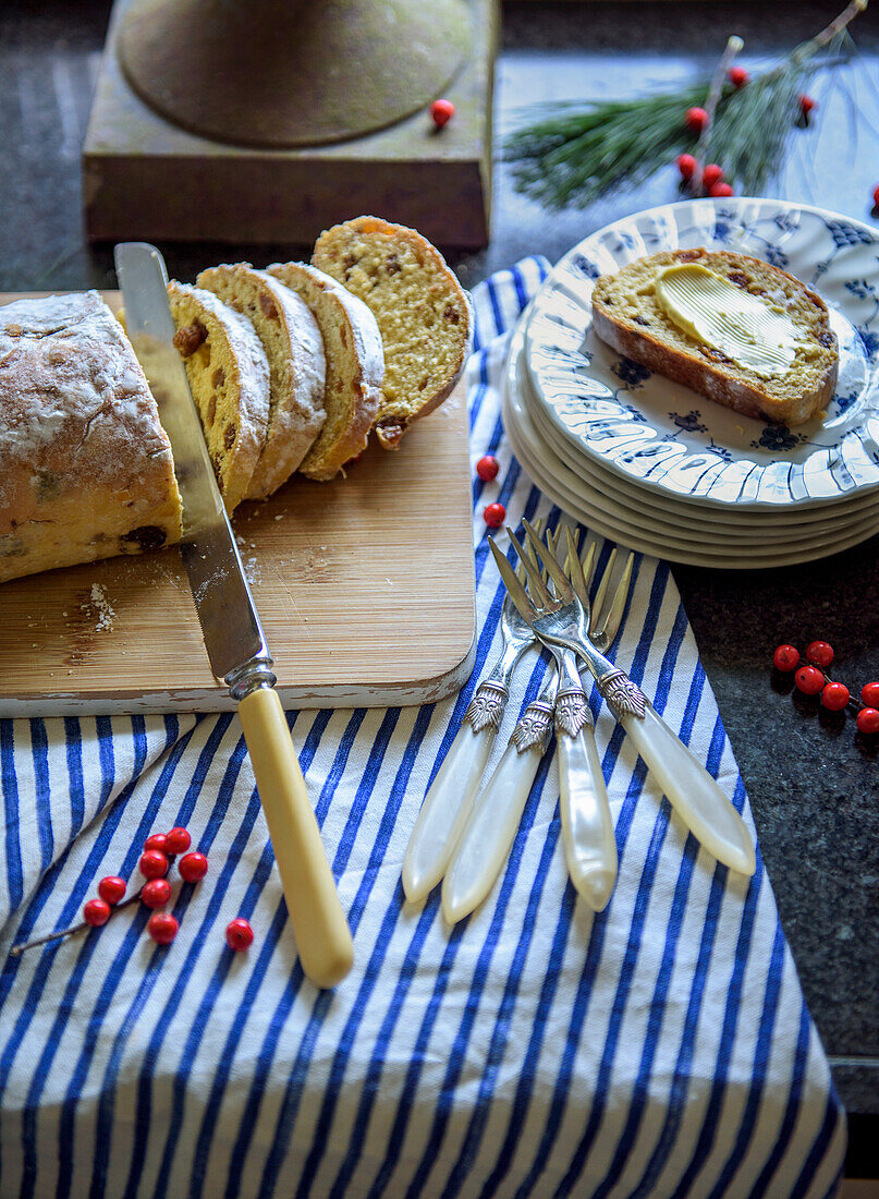 Sliced stollen on a wooden board, plates and cutlery on a striped cloth