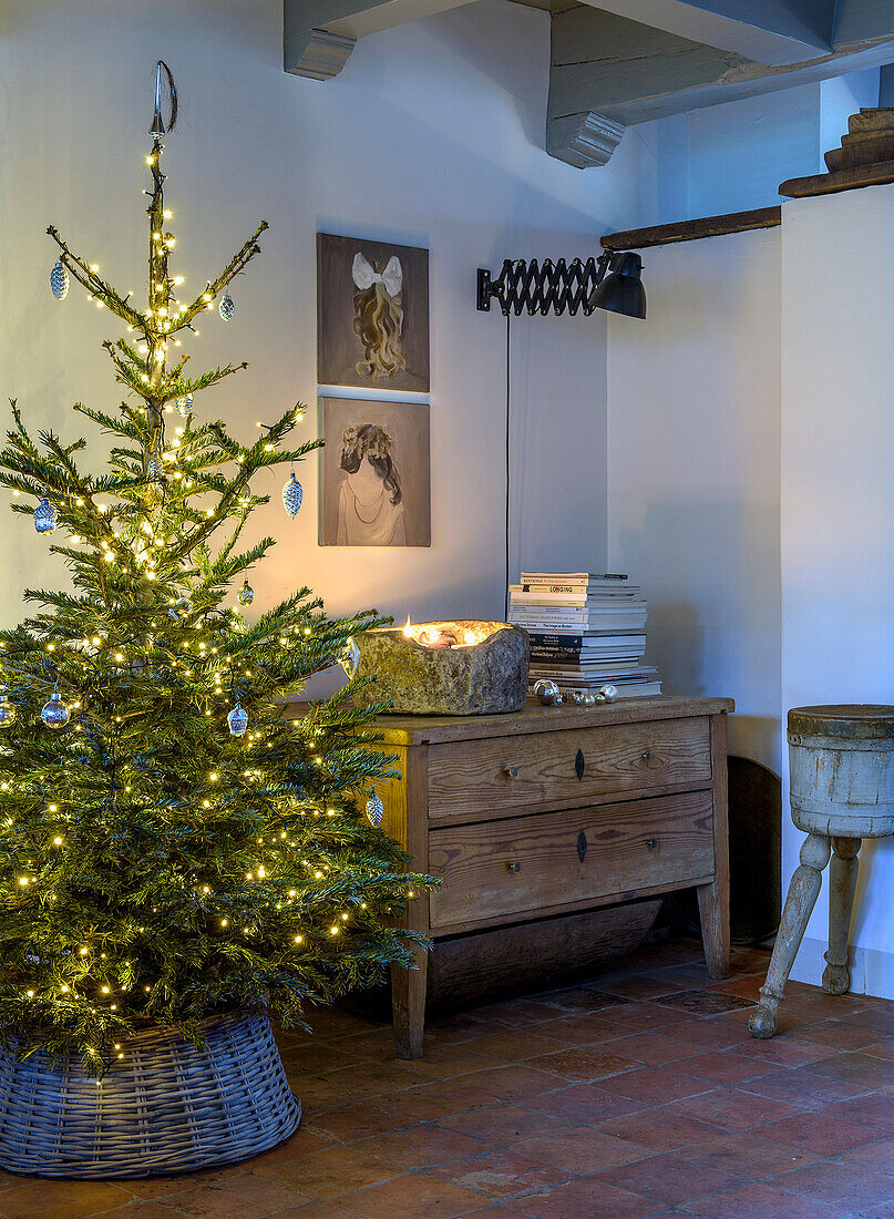 Illuminated Christmas tree next to rustic chest of drawers and wall pictures