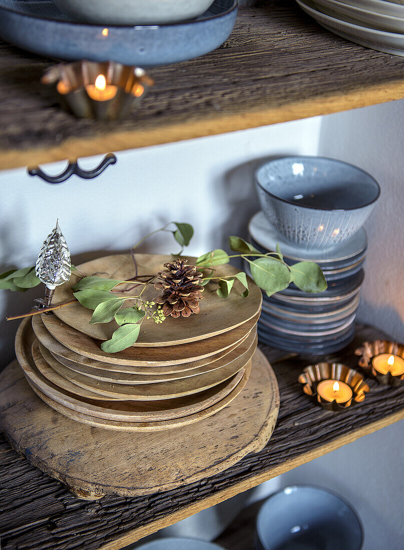 Stacked wooden plates and bowls on a rustic shelf, decorated with tea lights and twigs