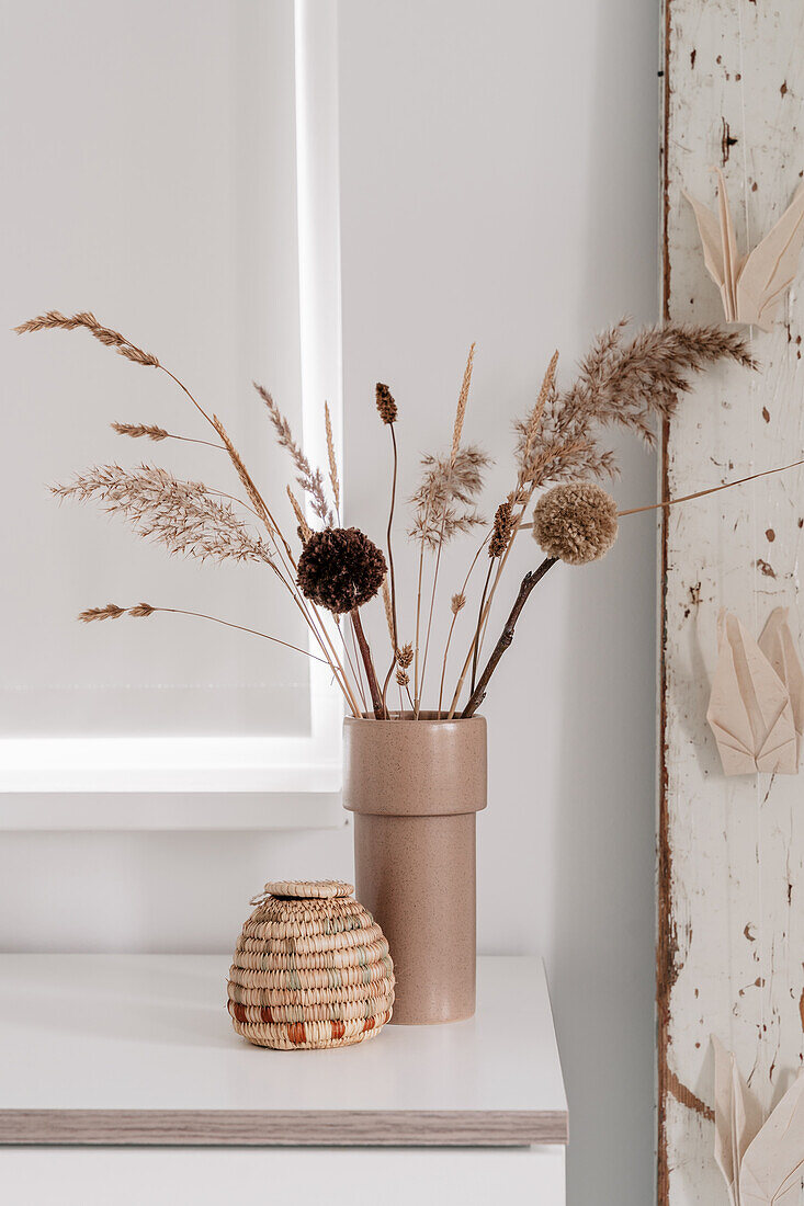 Trockenblumenarrangement und Pompons in beigefarbener Vase auf weißem Tisch