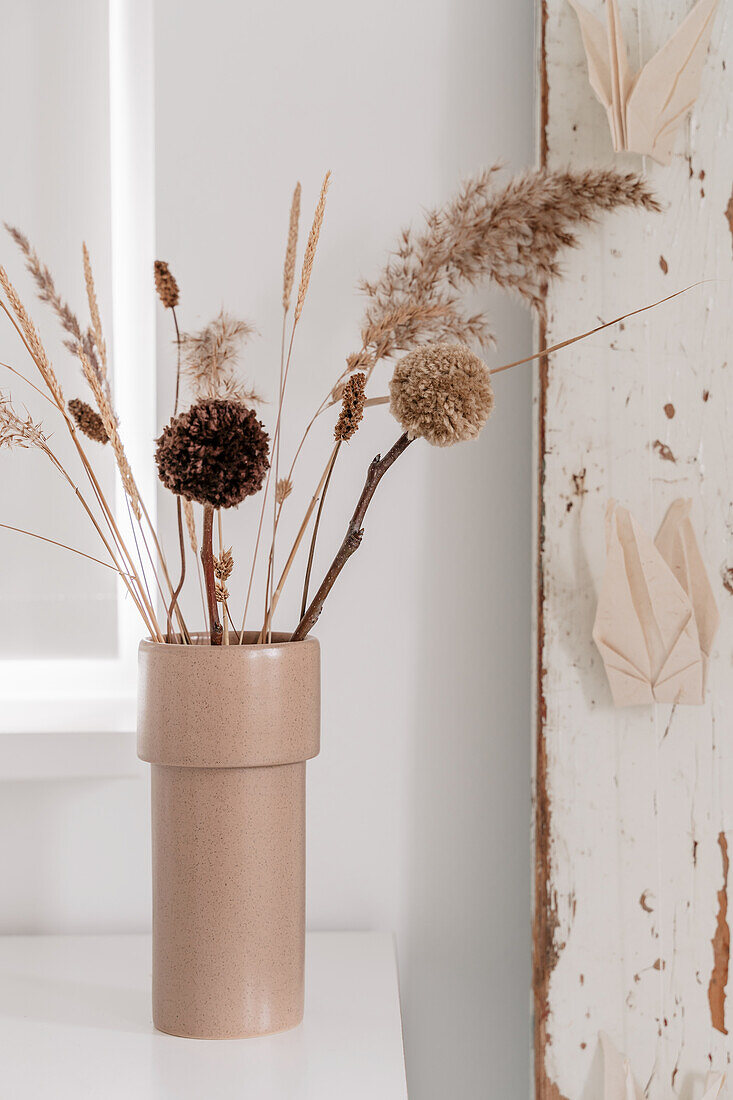 Dried flowers and pompoms in a beige-coloured vase on a white table