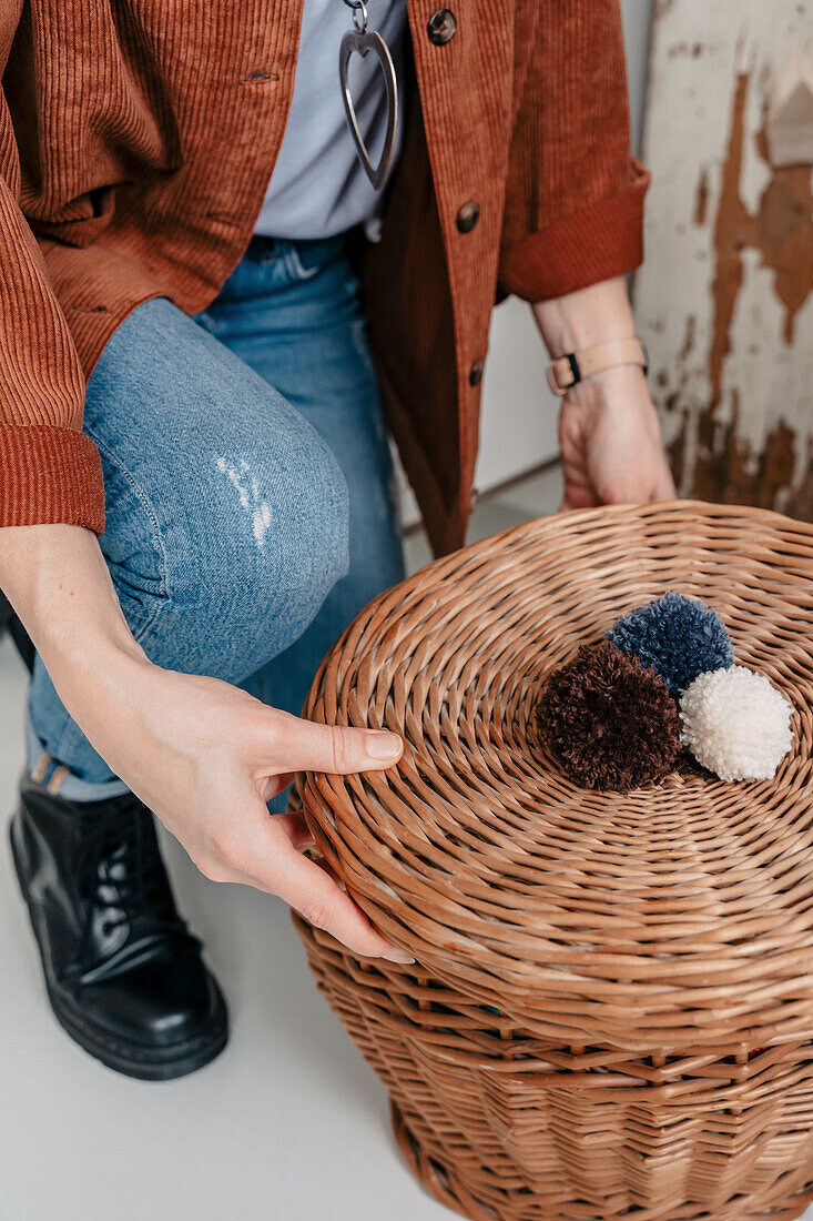 Person arranges a woven basket lid with three colourful pompoms