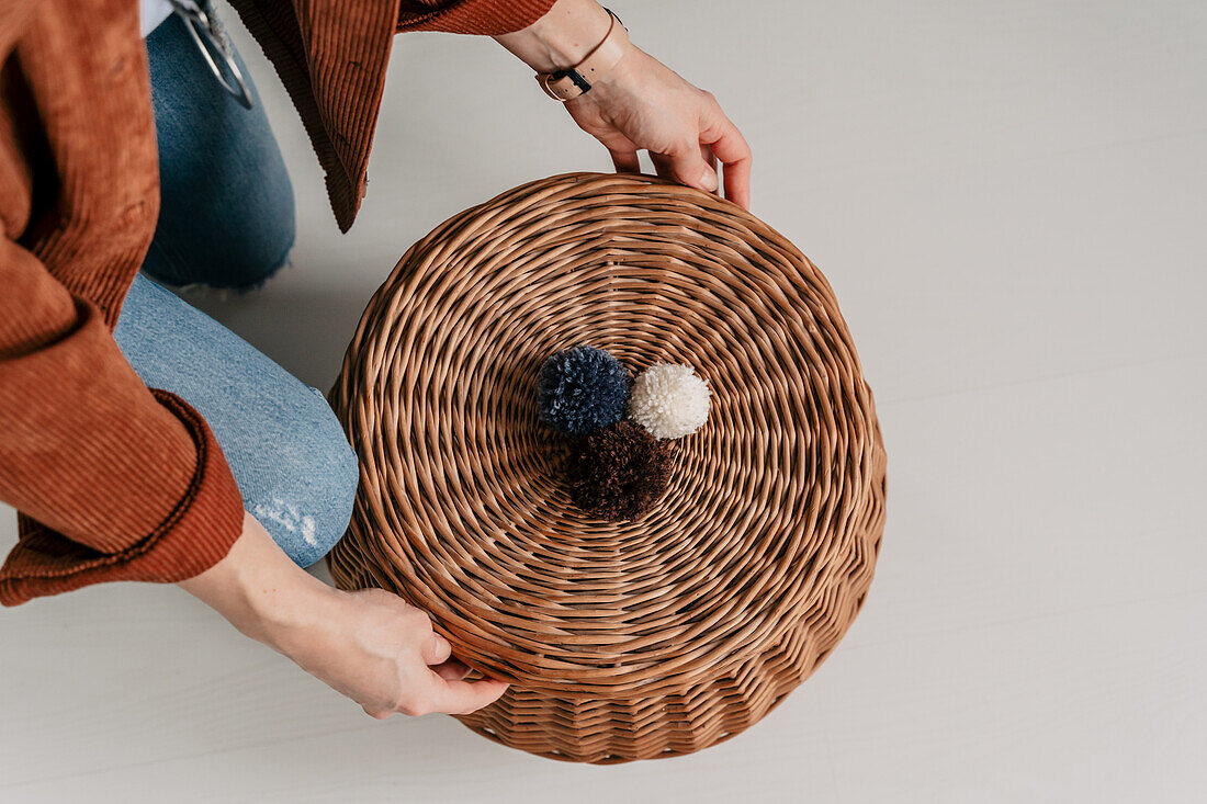 Woven basket with three woollen pompoms in blue, white and brown