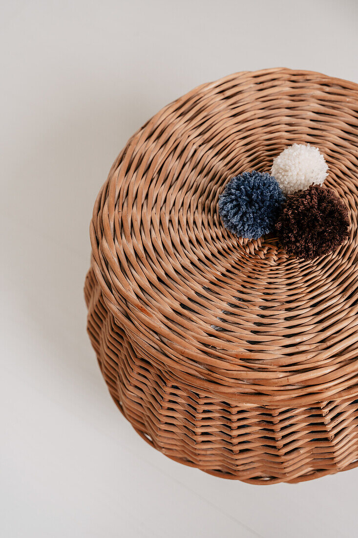 Woven basket with three pompoms in blue, white and brown