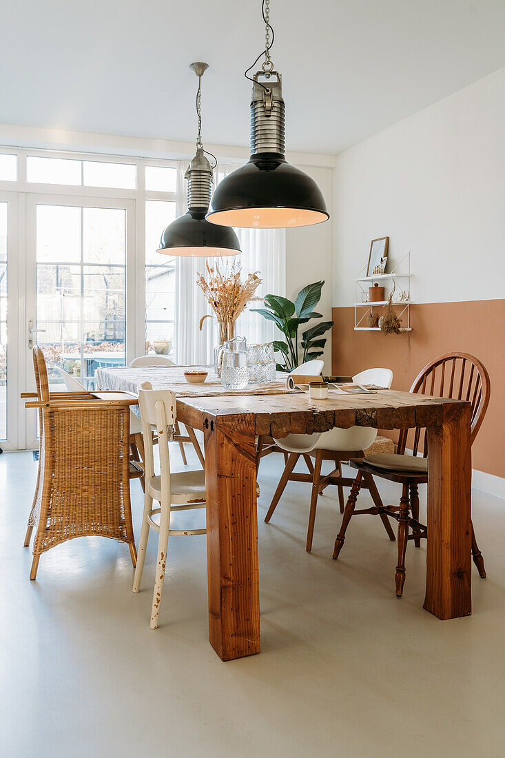 Dining room with wooden table, mixed chairs and plants in the background