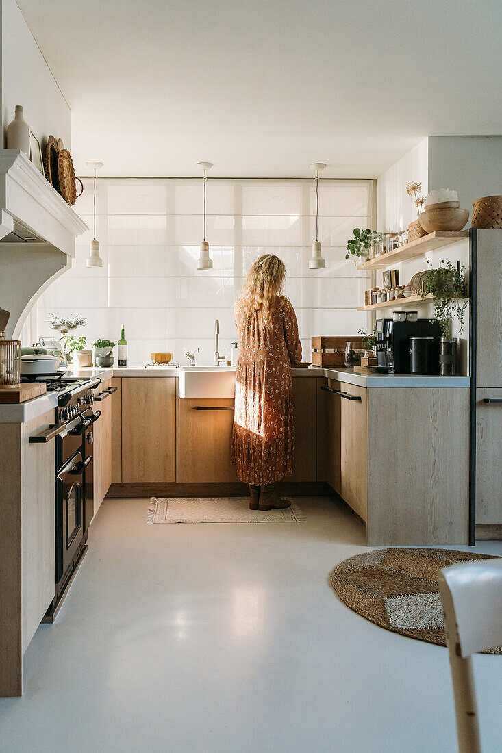 Woman standing in light-coloured kitchen with wooden fronts and open shelves